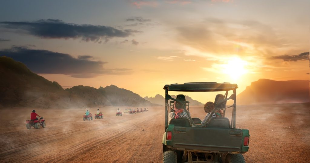 A line of quad bikes parked atop a high sand ridge in Dubai at sunset, with long shadows stretching across the rippled dunes.