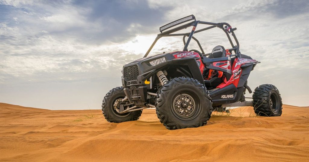 Can-Am buggy parked at a Dubai desert safari camp during sunset.